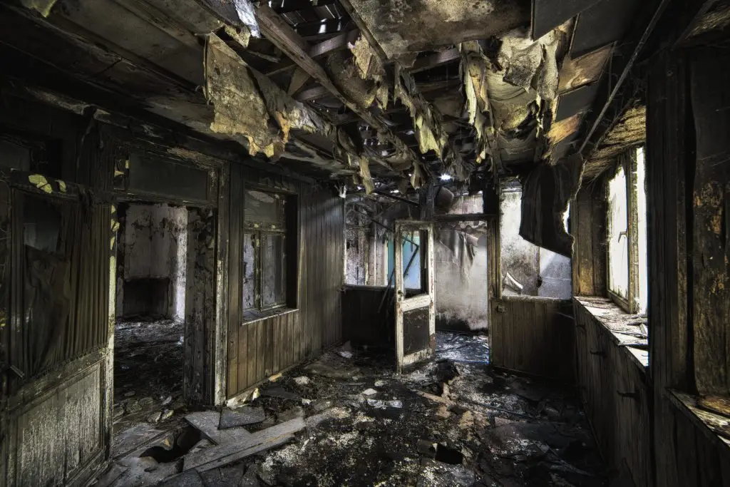 Inside view of an abandoned building with burned walls and damaged doors, showcasing fire damage restoration challenges